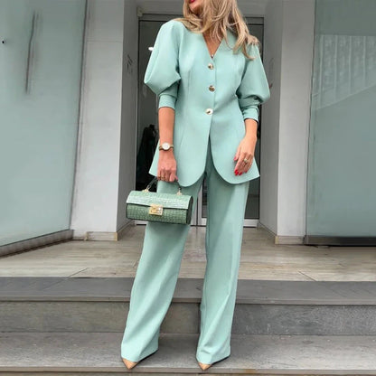 Frau in mintgrünem Hosenanzug mit Puffärmeln und Knöpfen, hält eine passende Handtasche. Elegante Mode, Business-Outfit, stilvoller Look.