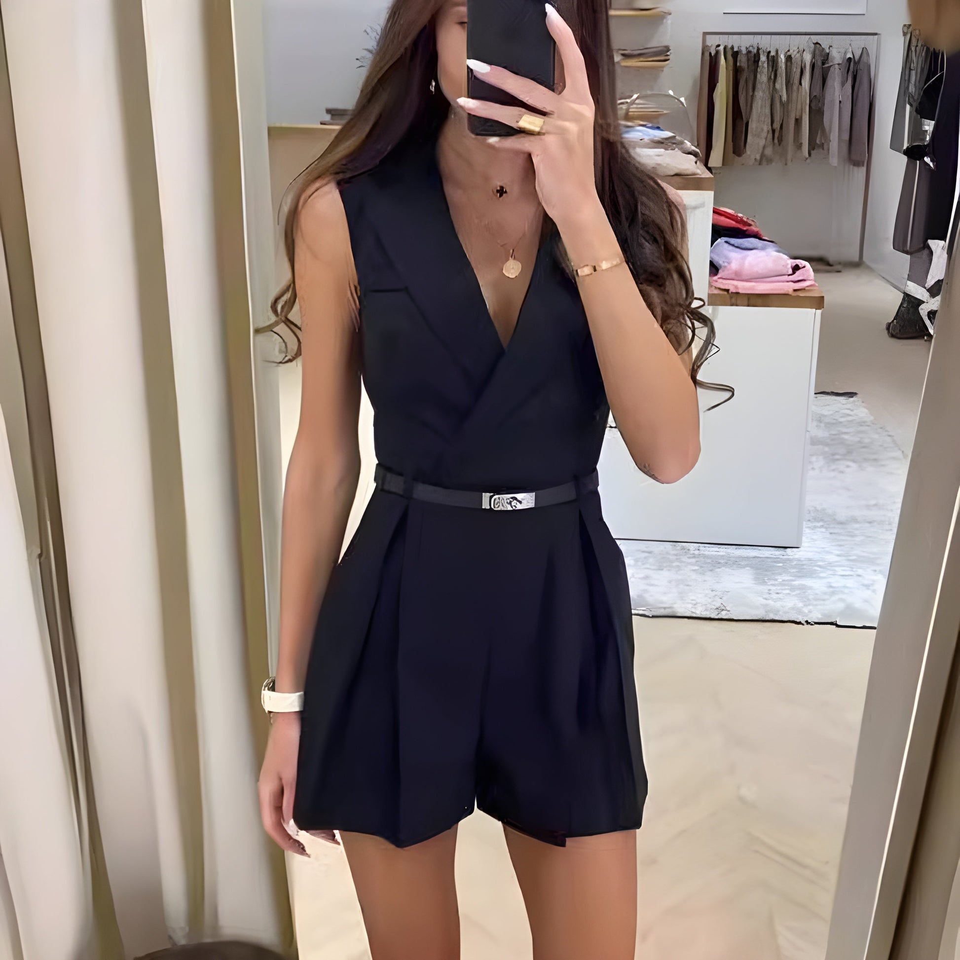 Frau in schwarzem ärmellosen Jumpsuit macht Selfie in Umkleidekabine. Modetrend, eleganter Look, stilvolle Damenmode, Shopping-Erlebnis.