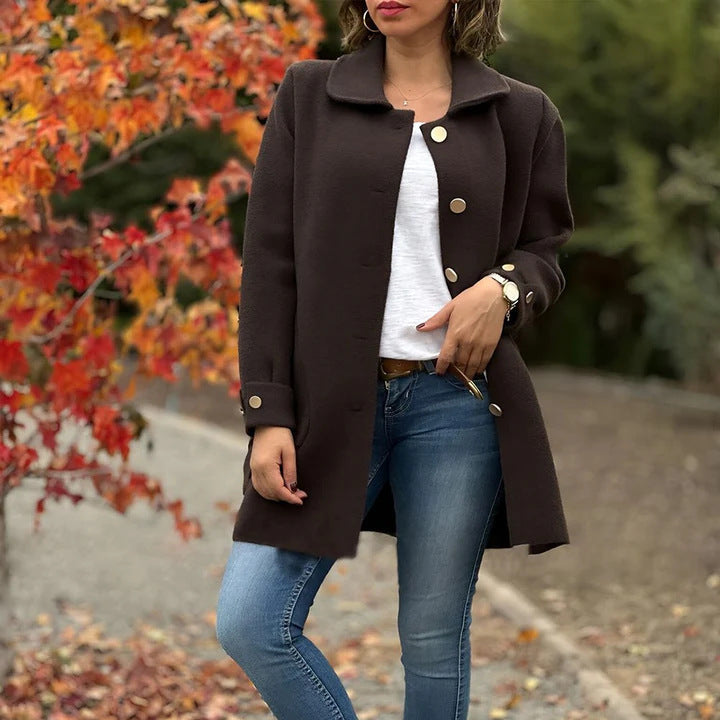 Frau in braunem Mantel und blauer Jeans vor herbstlichen Bäumen. Modischer Herbstlook, stilvolle Damenbekleidung, Outdoor-Mode.
