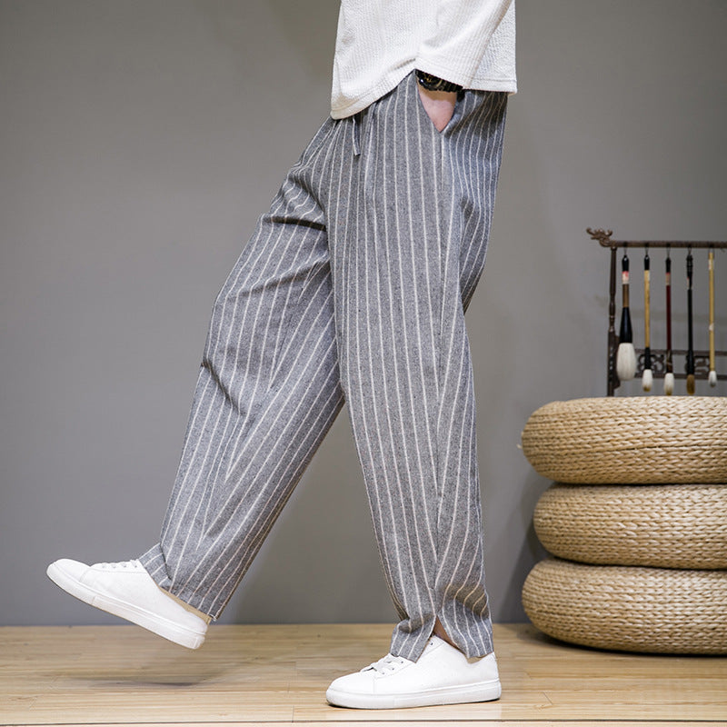 Graue gestreifte Herren-Leinenhose, locker geschnitten, kombiniert mit weißen Sneakers. Ideal für lässige Mode und Sommeroutfits.