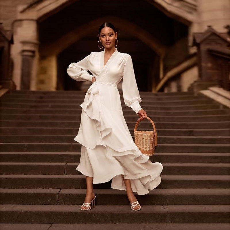 Frau in elegantem weißen Kleid mit Rüschen steht auf Treppe, hält einen Korb. Mode, Abendkleid, stilvoll, elegant, Damenmode, Accessoires.
