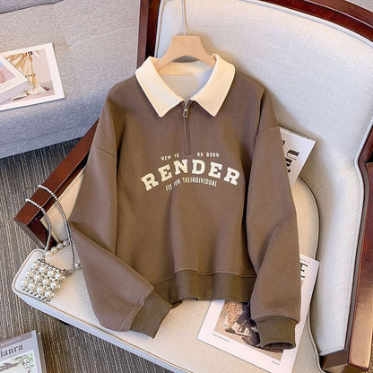 Brauner Pullover mit weißem Kragen und Reißverschluss, Aufschrift "RENDER", auf einem Sessel liegend, daneben eine Perlenhandtasche und Zeitschriften.
