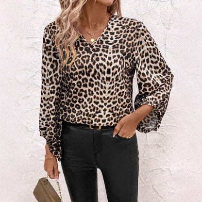 Frau in Leopardenmuster-Bluse und schwarzer Hose vor weißer Wand. Modetrend, Damenmode, stilvolles Outfit, lässiger Look, Accessoires.