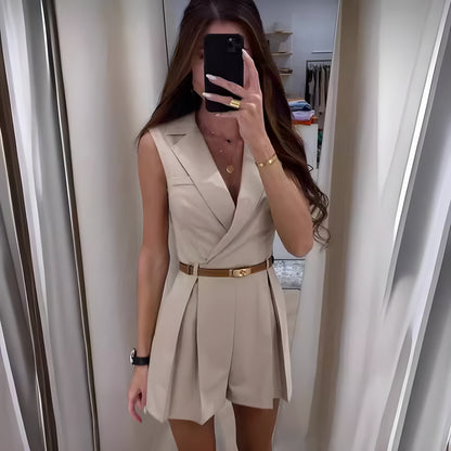 Frau in beigem ärmellosen Jumpsuit mit Gürtel, Spiegel-Selfie, modisches Outfit, elegantes Design, lange Haare, goldene Accessoires.