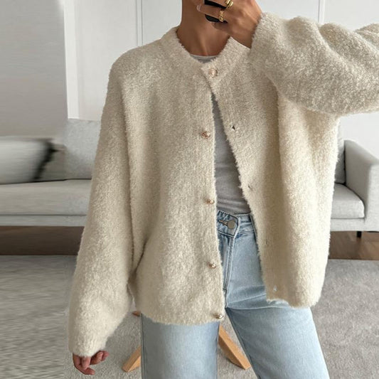 Person trägt eine cremefarbene, flauschige Strickjacke über einem weißen T-Shirt und hellblauen Jeans. Modetrend, gemütlicher Look, Herbstmode.