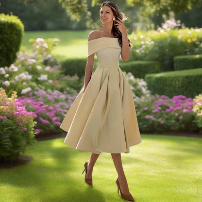 Frau im eleganten, cremefarbenen Kleid spaziert durch blühenden Garten, umgeben von grünen Hecken und bunten Blumen, Sommermode, Natur.
