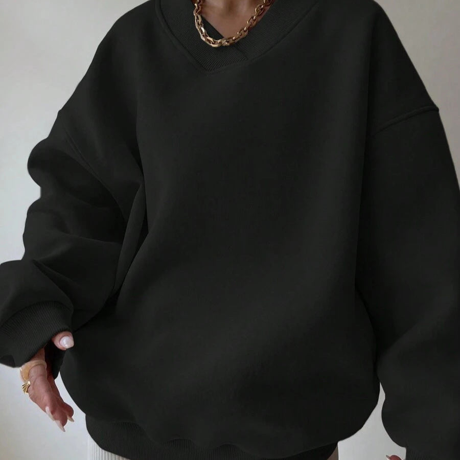 Dunkler Oversize-Pullover, lässig getragen, mit goldener Halskette. Modetrend, bequeme Kleidung, minimalistischer Stil.