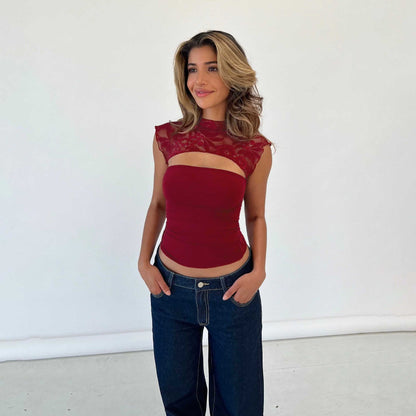 Junge Frau in rotem Spitzenoberteil und blauer Jeans vor weißem Hintergrund, lächelnd. Mode, Damenbekleidung, Freizeitlook.
