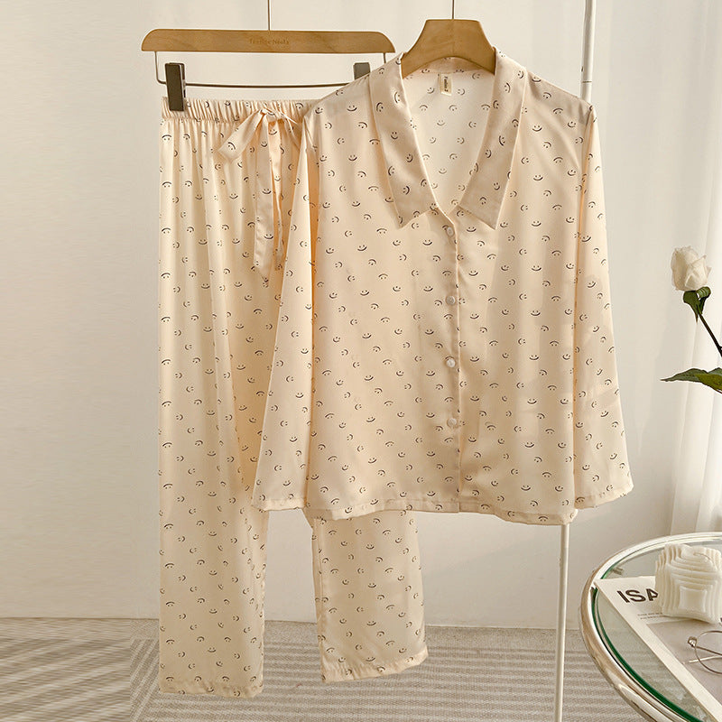 Beige Damen-Pyjama-Set aus Satin mit dezentem Muster, bestehend aus langärmligem Hemd und Hose, auf Holzkleiderbügeln in modernem Schlafzimmer.