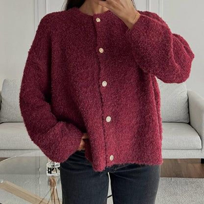 Frau trägt roten Strick-Cardigan mit Knöpfen, gemütlich und modisch, vor grauem Sofa. Perfekt für Herbstmode und lässige Outfits.