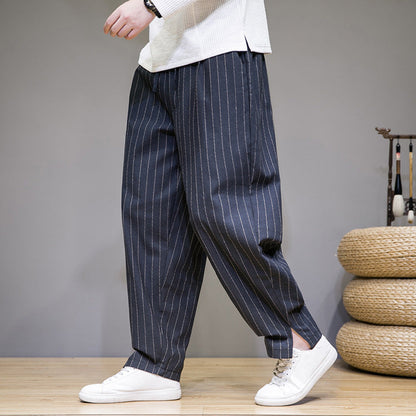 Person trägt weite, gestreifte Haremshose in Dunkelblau mit weißen Streifen, kombiniert mit weißen Sneakers. Modetrend, lässiger Stil, Herrenbekleidung.