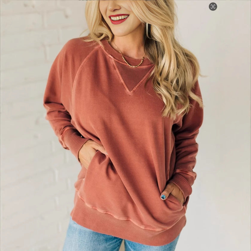 Frau in rotem Sweatshirt und blauer Jeans vor weißer Ziegelwand, lächelnd. Modetrend, lässiger Stil, Herbstmode, Damenbekleidung.