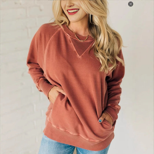 Frau in rotem Sweatshirt und blauer Jeans vor weißer Ziegelwand, lächelnd. Modetrend, lässiger Stil, Herbstmode, Damenbekleidung.