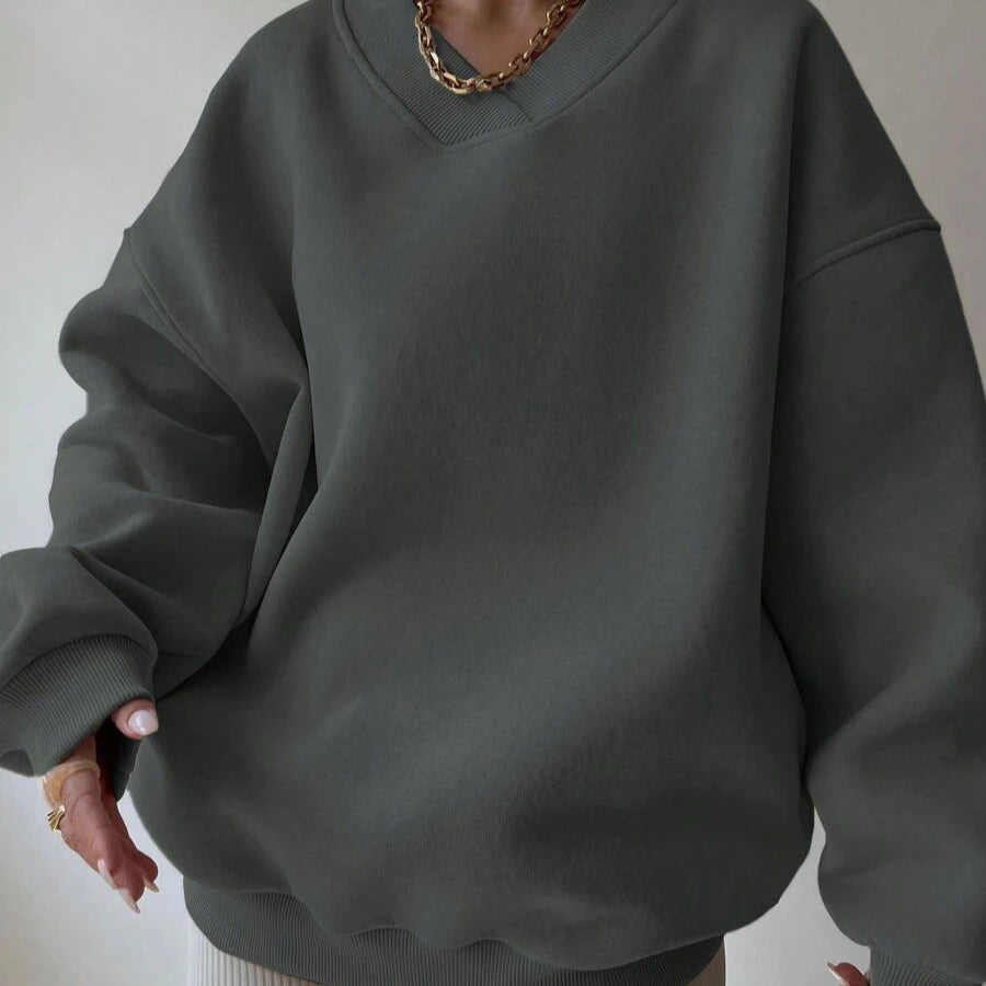 Dunkelgrauer Oversize-Pullover aus Baumwolle, getragen von Person mit goldener Halskette. Modetrend, lässiger Stil, bequeme Kleidung.
