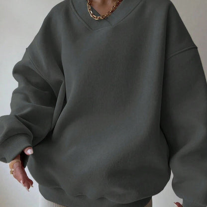 Dunkelgrauer Oversize-Pullover aus Baumwolle, getragen von Person mit goldener Halskette. Modetrend, lässiger Stil, bequeme Kleidung.