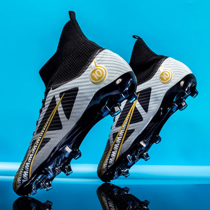 Zwei moderne Fußballschuhe mit Stollen, schwarz-weiß mit goldenen Akzenten, vor blauem Hintergrund. Ideal für Rasenplätze, sportliches Design.