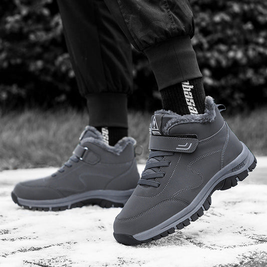 Graue Winterstiefel mit Fellfutter auf Schnee, getragen von Person in schwarzer Hose. Outdoor-Schuhe, rutschfeste Sohle, warm, wasserdicht.