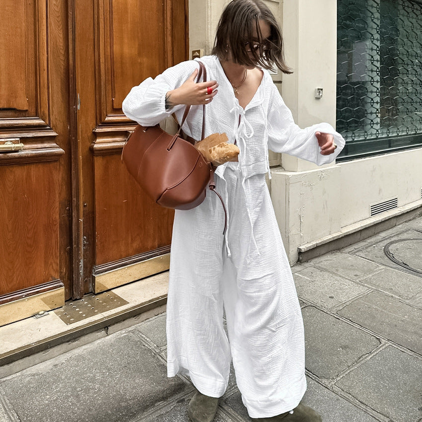Frau in weißem Kleid mit brauner Tasche und Baguette auf Pariser Straße. Modetrend, Streetstyle, Paris, lässig, elegant.