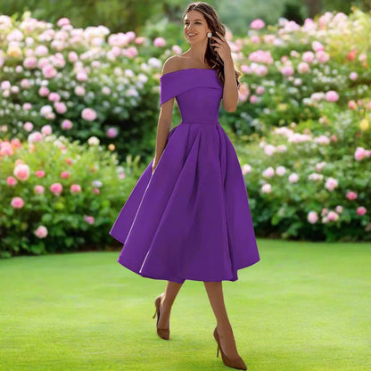Frau in lila Abendkleid im Garten, umgeben von blühenden Rosen. Elegantes Design, schulterfrei, knielang. Perfekt für Sommerveranstaltungen.