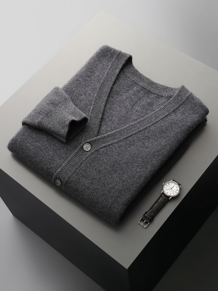 Grauer Kaschmir-Cardigan und Armbanduhr auf grauem Tisch. Luxuriöse Herrenmode, elegante Accessoires, stilvolle Kleidung, zeitloses Design.