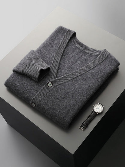 Grauer Kaschmir-Cardigan und Armbanduhr auf grauem Tisch. Luxuriöse Herrenmode, elegante Accessoires, stilvolle Kleidung, zeitloses Design.