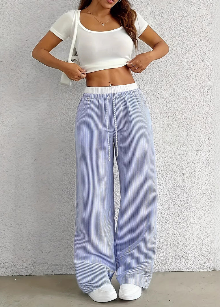 Frau in weißem Crop-Top und gestreifter, blauer Hose, lässiger Sommerlook, modische Freizeitkleidung, weiße Sneaker, trendige Damenmode.