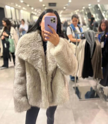 Frau in beigem Kunstpelzmantel macht Selfie in einem Bekleidungsgeschäft. Mode, Winterkleidung, Shopping, Spiegelselfie.