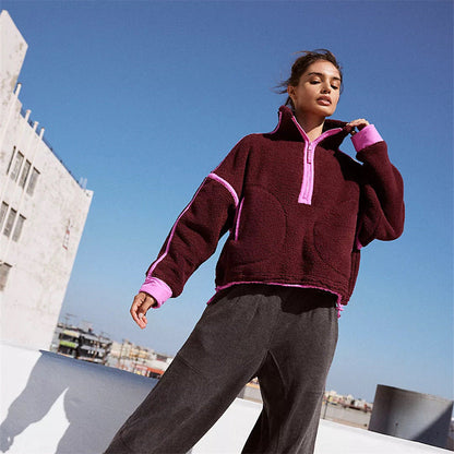 Frau in bordeauxfarbenem Fleece-Pullover mit rosa Akzenten, steht auf einem Dach. Modetrend, Herbstmode, urbaner Stil, lässige Damenbekleidung.