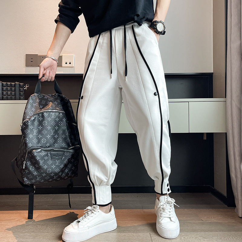 Mann in weißer Jogginghose mit schwarzen Streifen, hält Designer-Rucksack, trägt schwarze Uhr und weiße Sneaker. Moderne Herrenmode, Streetwear.