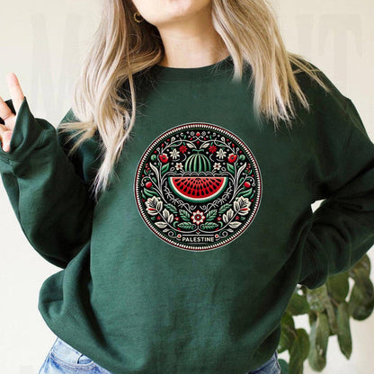 Frau trägt grünen Pullover mit palästinensischem Stickmuster, Wassermelonen-Design. Modetrend, Ethno-Mode, nachhaltige Kleidung.