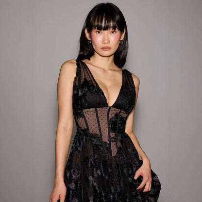 Eine Frau in einem eleganten, schwarzen Spitzenkleid mit tiefem Ausschnitt, posiert vor einem grauen Hintergrund. Mode, Abendkleid, Stil.