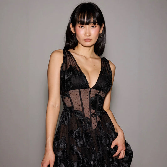 Eine Frau in einem eleganten, schwarzen Spitzenkleid mit tiefem Ausschnitt, posiert vor einem grauen Hintergrund. Mode, Abendkleid, Stil.