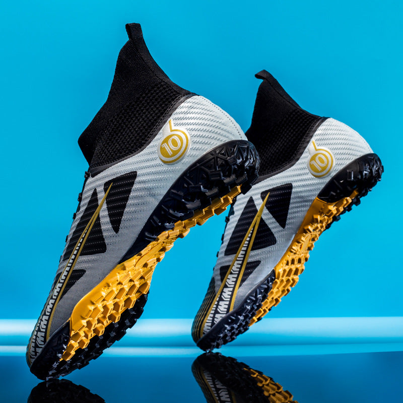 Graue und schwarze Fußballschuhe mit gelben Akzenten vor blauem Hintergrund, modernes Design, rutschfeste Sohle, ideal für Kunstrasen.