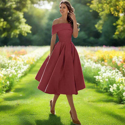 Frau in elegantem, schulterfreiem, rotem Kleid spaziert durch blühenden Garten. Sommermode, Abendkleid, Natur, stilvolle Kleidung.