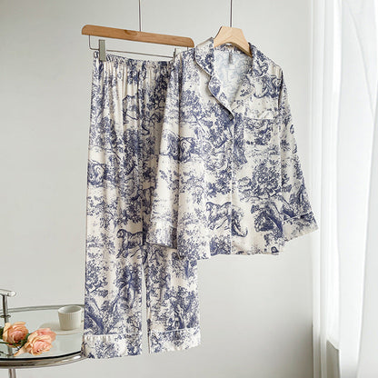 Zweiteiliger Pyjama-Set aus Seide mit blau-weißem Toile-de-Jouy-Muster, hängend auf Holzkleiderbügeln, neben einem Tisch mit Rosen und Tasse.