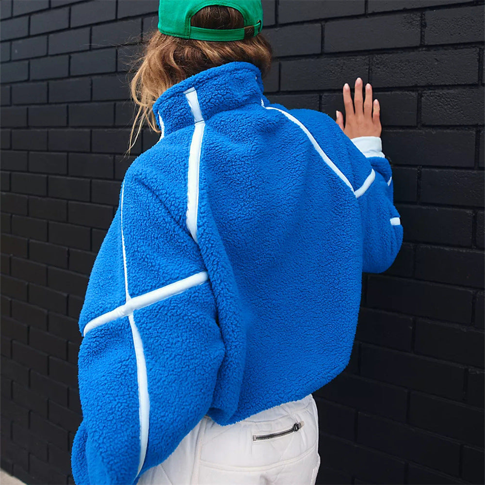 Frau in blauer Fleecejacke mit weißen Streifen, grüner Kappe, vor schwarzer Ziegelwand. Modetrend, Streetwear, Herbstmode.