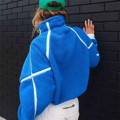 Frau in blauer Fleecejacke mit weißen Streifen, grüner Kappe, vor schwarzer Ziegelwand. Modetrend, Streetwear, Herbstmode.