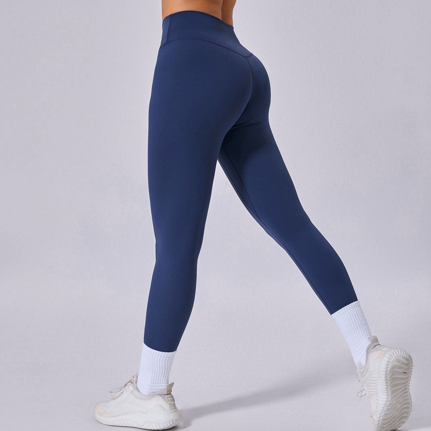 Damen in blauer Sportleggings und weißen Sneakers, Rückansicht. Fitnessmode, bequeme Sportbekleidung, trendige Leggings für Workout und Freizeit.