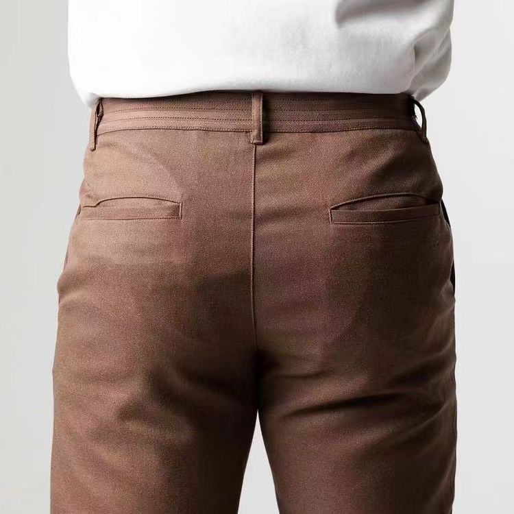 Herrenmode: Nahaufnahme einer braunen Anzughose aus Baumwolle, getragen von einer Person in weißem Hemd. Elegante Business-Kleidung für Herren.