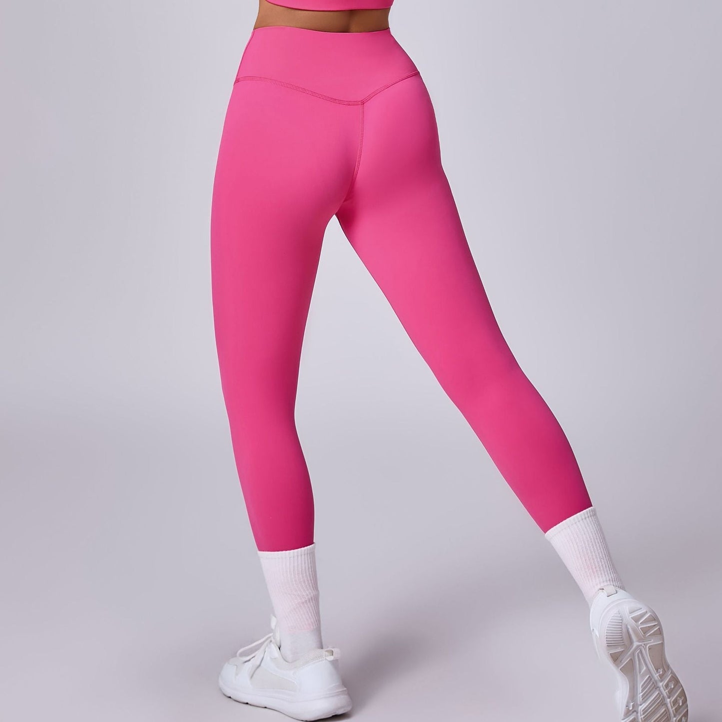 Frau in pinker Sportleggings und weißen Sneakers, Rückansicht. Fitnessmode, Sportbekleidung, athletischer Look, trendige Leggings.