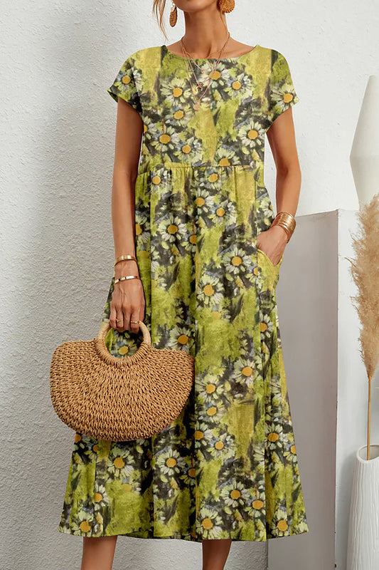 Frau in grünem, geblümtem Sommerkleid mit Gänseblümchenmuster, hält eine runde Strohtasche. Perfekt für lässige Sommermode und Strandoutfits.