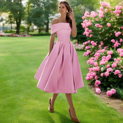 Frau in rosa Abendkleid im Garten, umgeben von blühenden Rosen und grünem Rasen. Elegantes, schulterfreies Design, ideal für Sommerveranstaltungen.