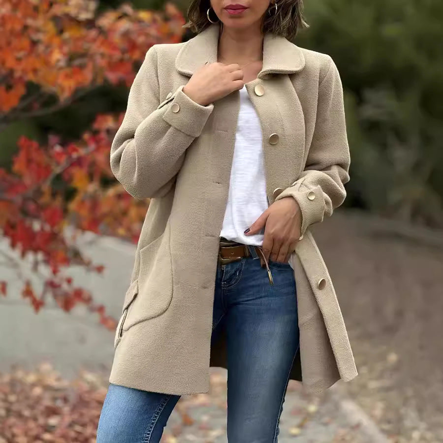 Frau in beigem Mantel und blauer Jeans vor herbstlicher Kulisse mit roten Blättern. Modetrend Herbst, stilvolle Damenbekleidung, Outdoor-Look.