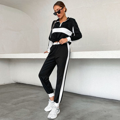 Frau in schwarz-weißem Trainingsanzug mit Sonnenbrille und weißen Sneakers, lehnt an weißer Wand. Sportmode, lässiger Stil, urbaner Look.