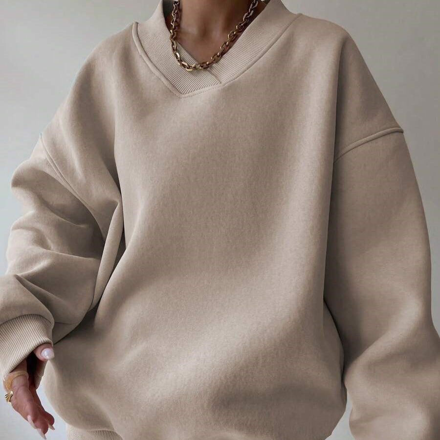 Beiger Oversize-Pullover aus Baumwolle, getragen von Person mit goldener Kette. Modetrend, lässiger Stil, gemütliche Kleidung, Herbstmode.