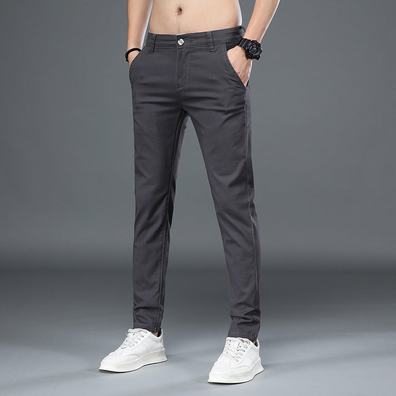 Mann trägt dunkelgraue Chinohose und weiße Sneaker vor grauem Hintergrund. Moderne Herrenmode, lässiger Stil, elegante Freizeitkleidung.