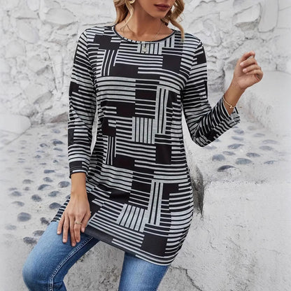 Frau in gestreiftem, geometrischem Langarmshirt und blauer Jeans sitzt auf einer weißen Steinbank. Modetrend, Damenmode, Freizeitlook.