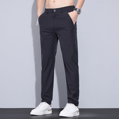 Mann trägt schwarze Chinohose und weiße Sneaker, Hände in den Taschen, vor grauem Hintergrund. Elegante Herrenmode, lässiger Stil.