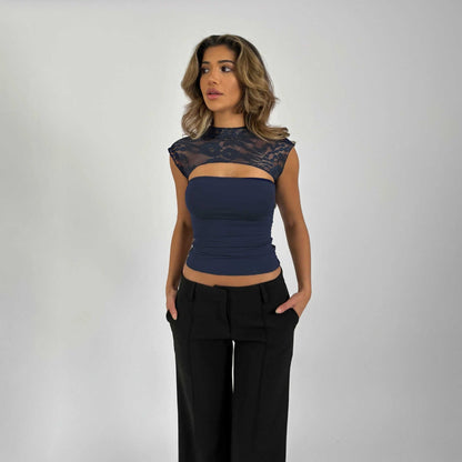 Frau in eleganter, ärmelloser Bluse mit Spitzenbesatz und schwarzer Hose vor grauem Hintergrund. Mode, Damenbekleidung, stilvolles Outfit.