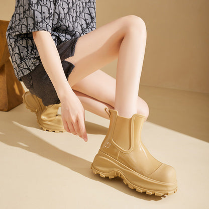 Frau trägt beige Gummistiefel mit dicker Sohle, kniet auf hellem Boden. Modische Regenstiefel, ideal für Herbstmode und Outdoor-Aktivitäten.